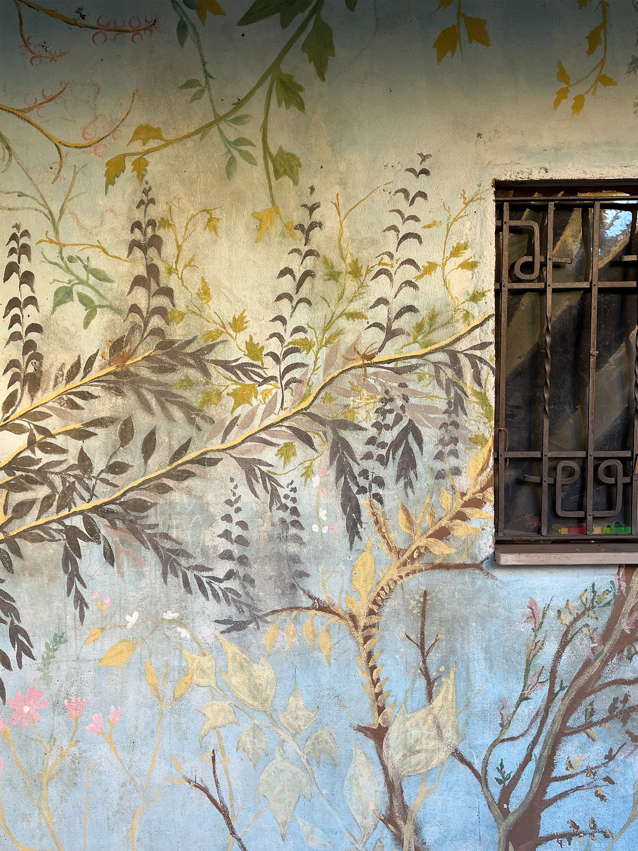 Decorative wall with floral and branch patterns and a window with bars.