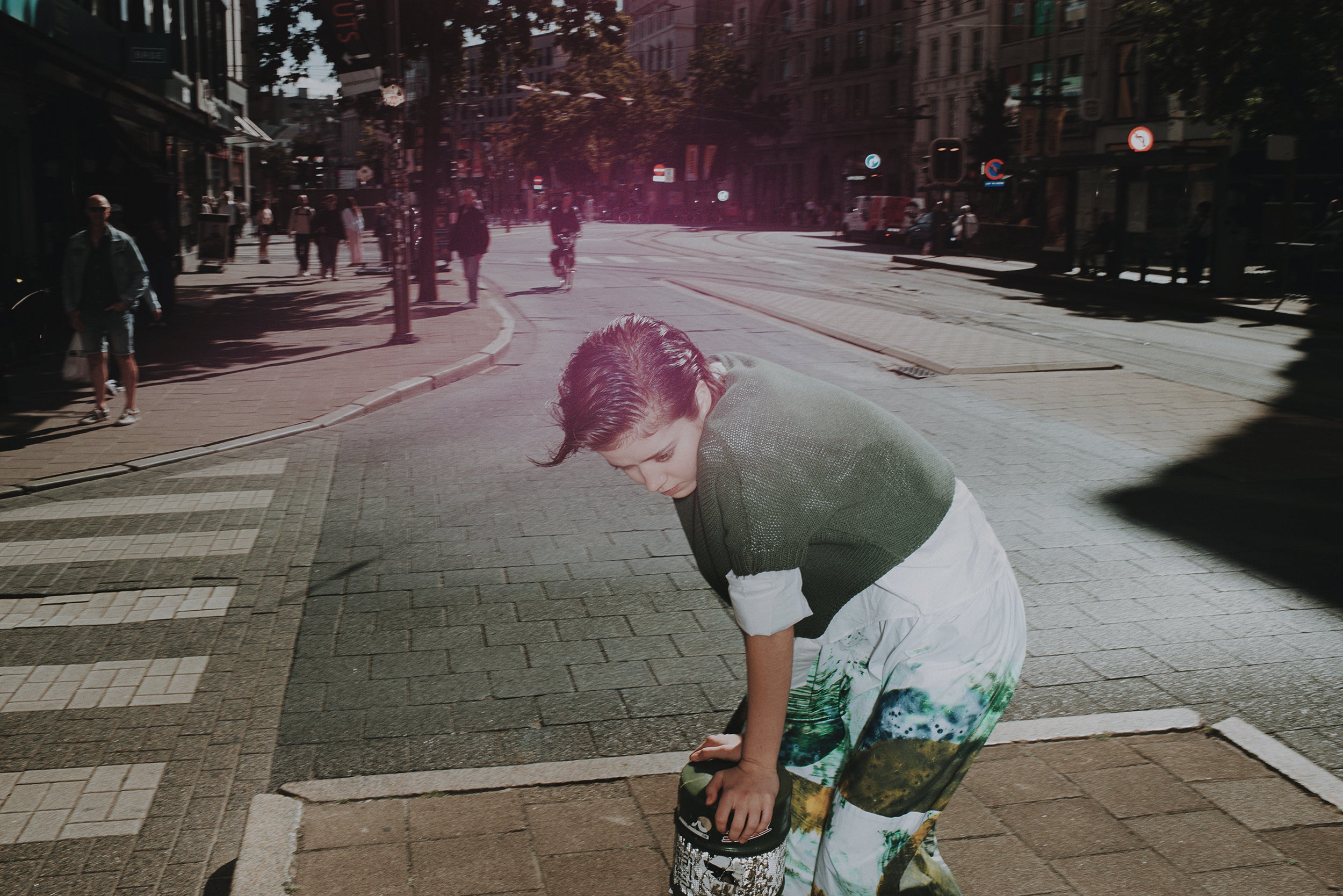 Person bending over a trash can on a city street