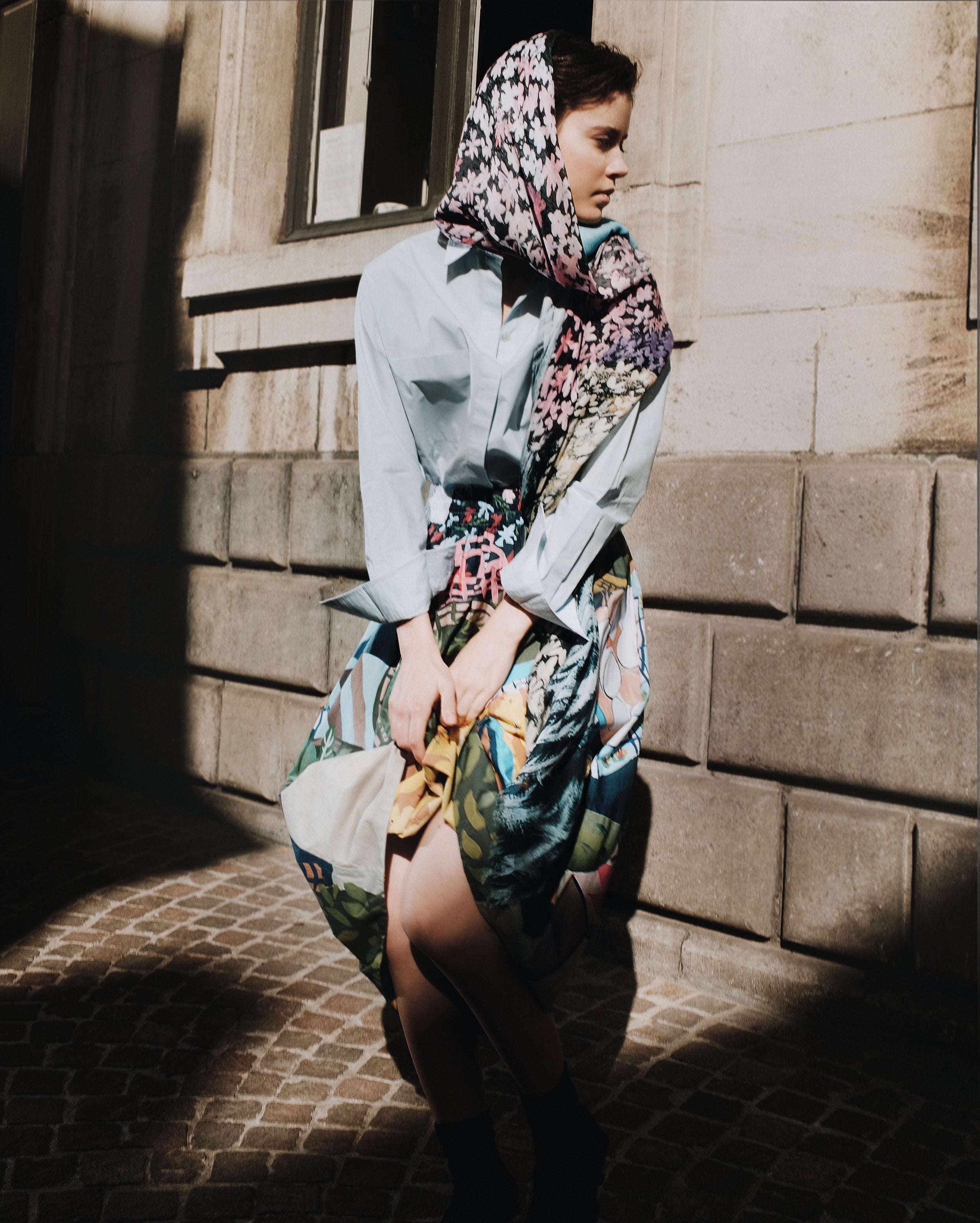 Woman wearing a colorful headscarf and dress standing on a stone pavement.