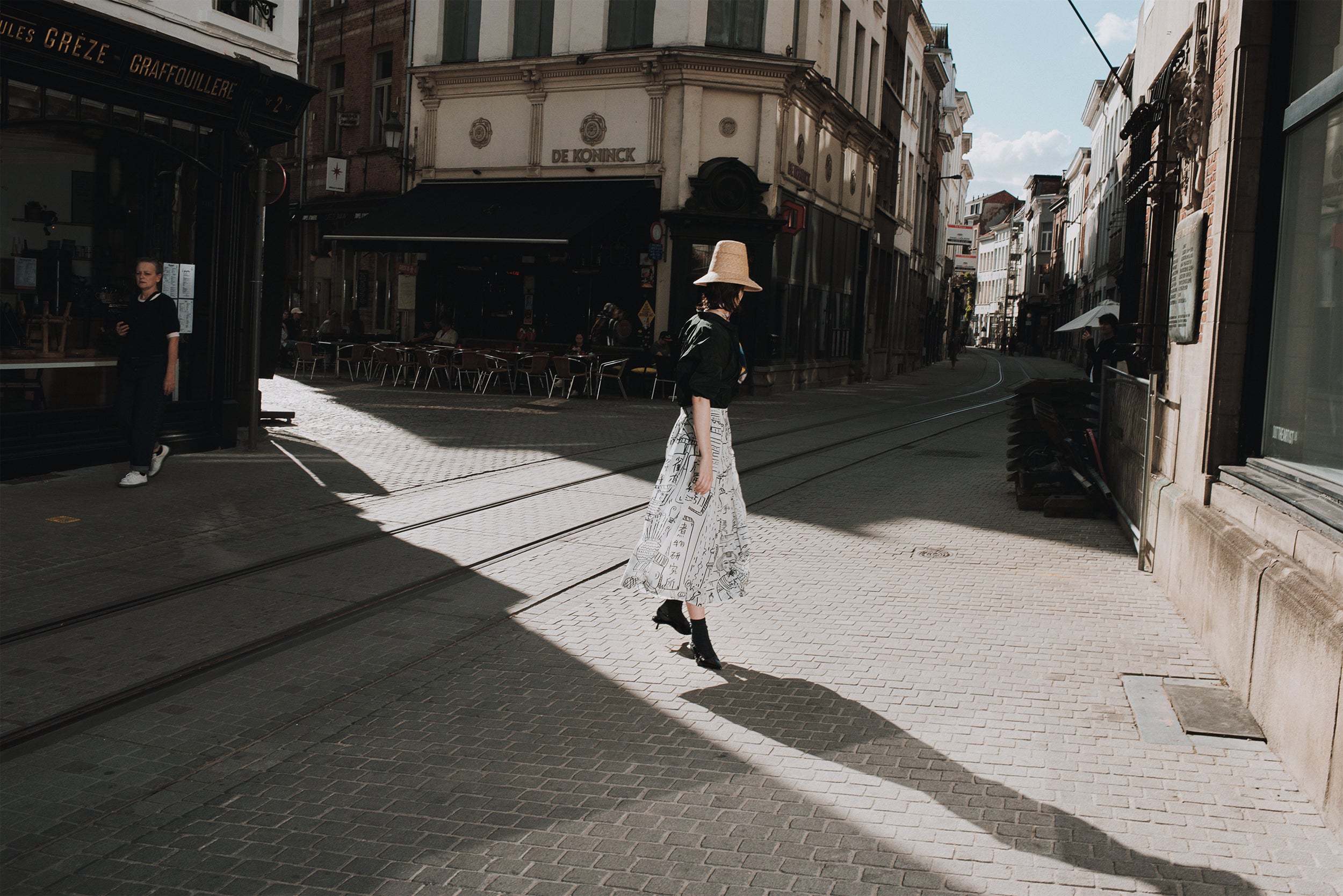 Woman walking on a sunlit street with buildings and a cafe in the background
